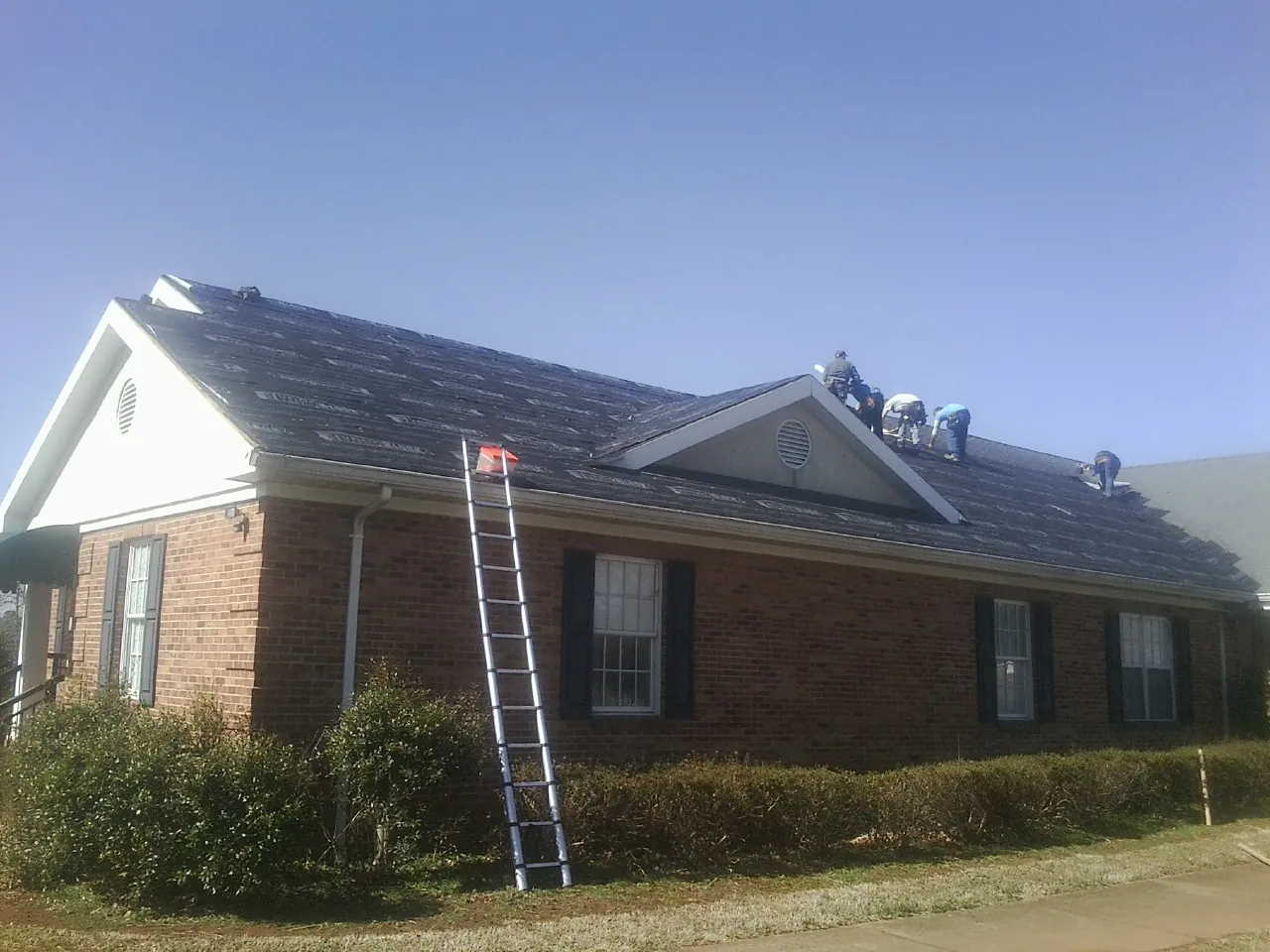Crew tearing shingles off a brick ranch roof with a ladder set — Emergency Roof Repair work by our crew in New Gloucester