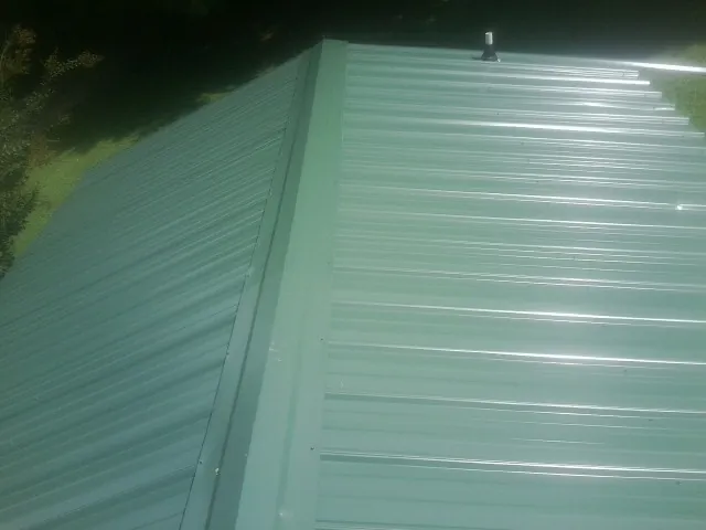 New green metal panels meeting at the ridge of a roof — Flat Roof Repair work by our crew in New Gloucester