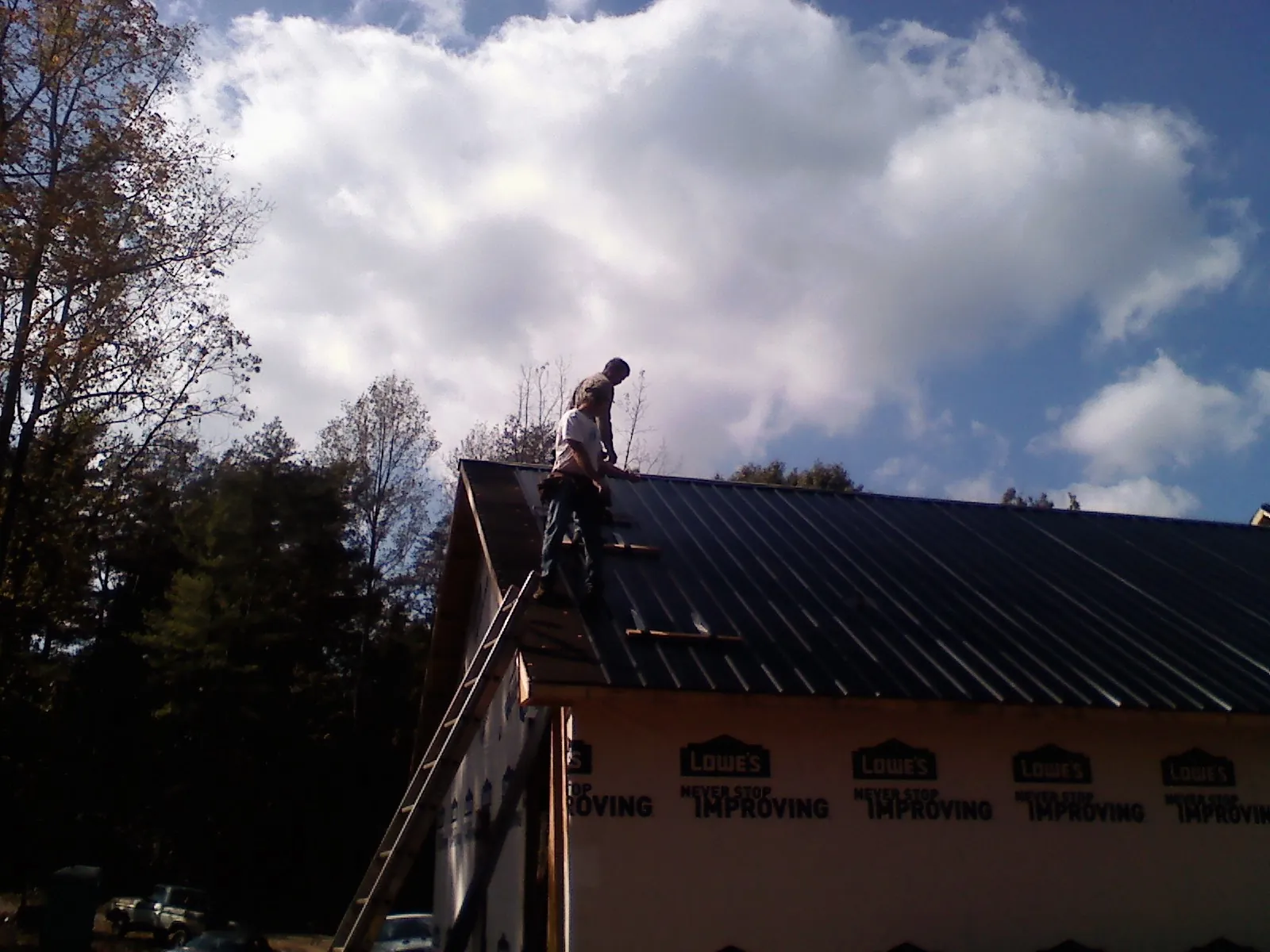 Roofer fastening dark metal panels high against a cloudy sky, from a Roof Inspection job in New Gloucester