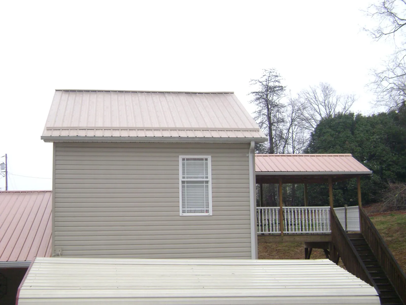 Tan metal roofs on a two story addition and attached porch, from a Roof Replacement job in New Gloucester